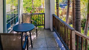 A covered outdoor area with a table and chairs, a railing, and a view of palm trees and greenery. - North Park Haven Summ (San Diego)
