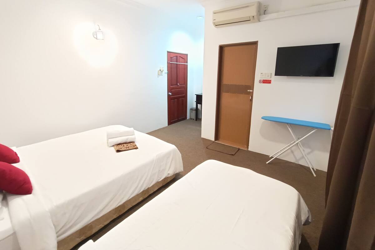 Habitación de hotel con dos camas individuales, un televisor montado en la pared, un aire acondicionado y una puerta que da a otra habitación.