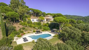 Una casa grande con piscina, rodeada de exuberante vegetación y árboles.