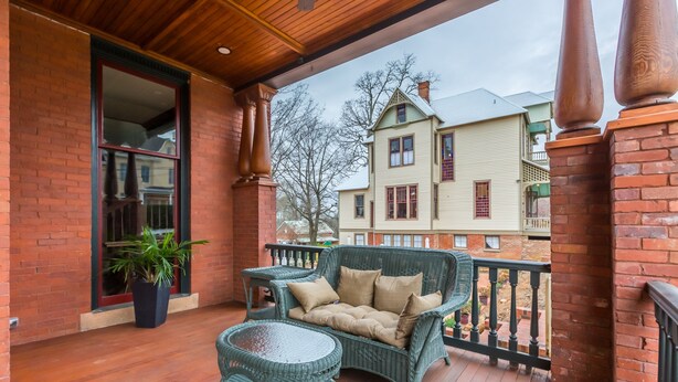 A wooden balcony with wicker furniture and a potted plant. - King Suite in Boutique Inn (Winston-Salem)