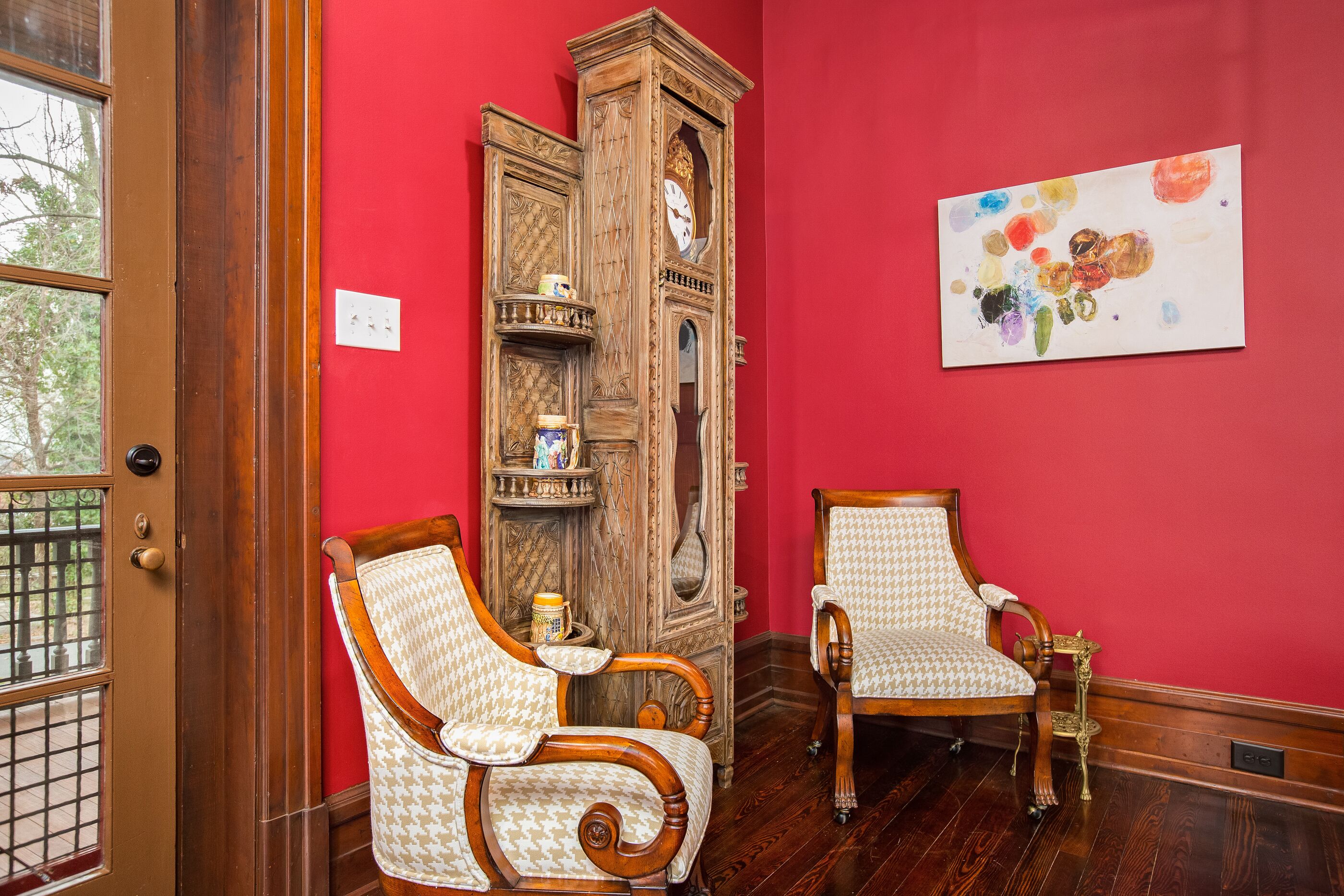 Een kamer met twee houten stoelen, een houten kast en een rode muur.