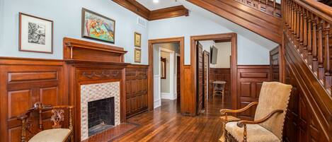 A spacious room with a wooden staircase, a fireplace, and two antique chairs.