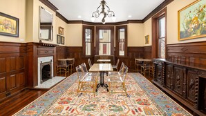 A dining room with a large table, clear chairs, a patterned carpet, wooden paneling, and a chandelier.