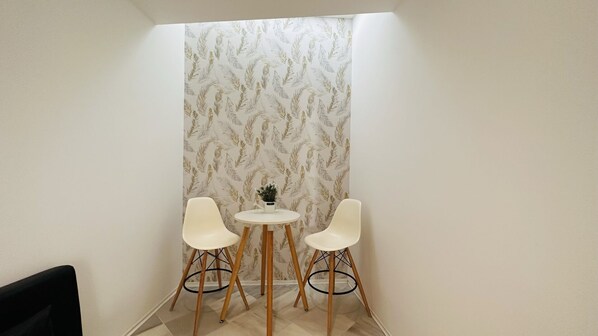 A small, modern room with two white chairs around a small round table, a potted plant on the table, and a patterned wallpaper.