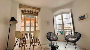 Ein Zimmer mit Tisch, Stühlen, einer Lampe und zwei Fenstern mit Blick auf Gebäude.
