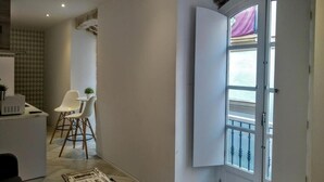 A modern kitchen with white cabinets, a dining area with a white chair, and a large window with a view. - Apto. 1 Dorm. Ext. 2ª Planta (Cádiz)