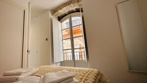 A bedroom with a bed, a window with a view of buildings, and a wardrobe. - Apto. 1 Dorm. Ext. 2ª Planta (Cádiz)