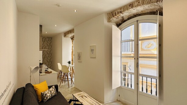 A modern living room with a sofa, a coffee table, and a dining area with chairs. - Apto. 1 Dorm. Ext. 2ª Planta (Cádiz)