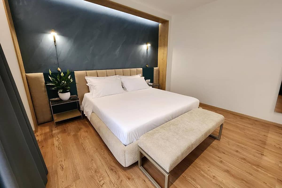 A modern bedroom with a large bed, bedside tables, a bench, and a potted plant.