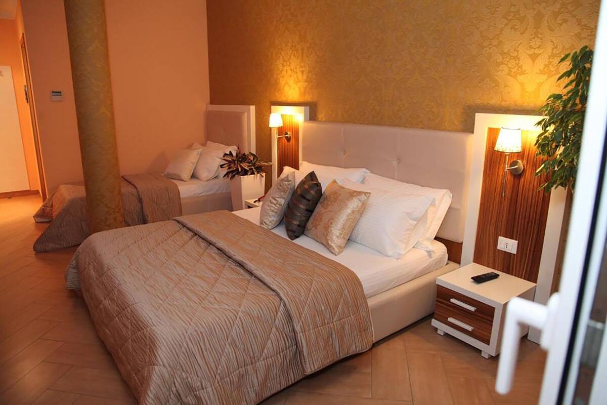 A hotel room with two beds, a nightstand with a lamp, and a small table with a phone.