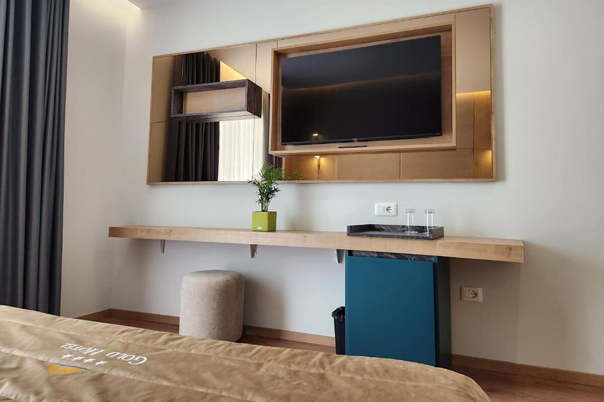 Una habitación de hotel moderna con cama, televisor montado, planta pequeña y zona de escritorio.