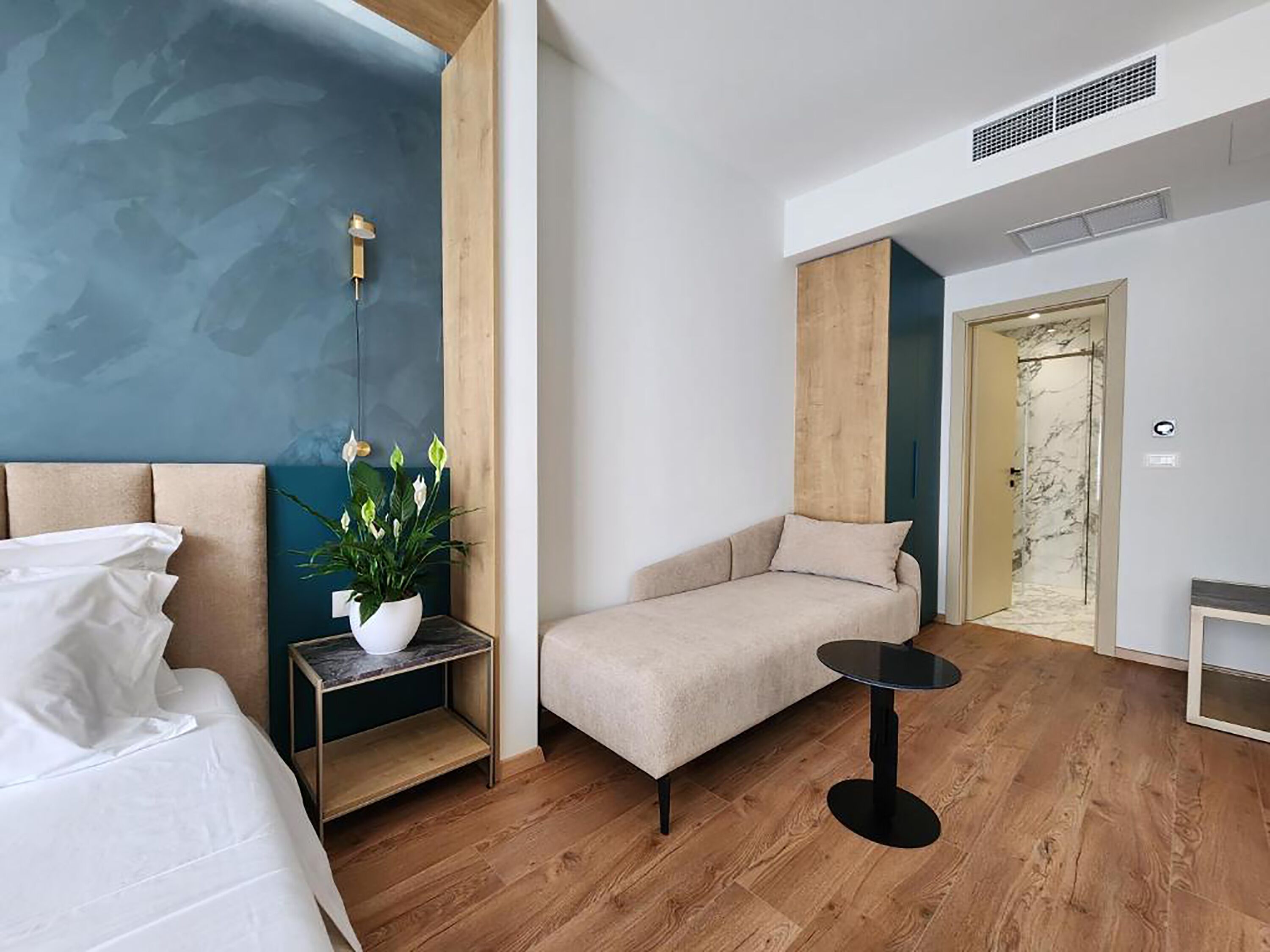 Una habitación de hotel moderna con una cama, un sofá, una mesita y una planta en maceta.