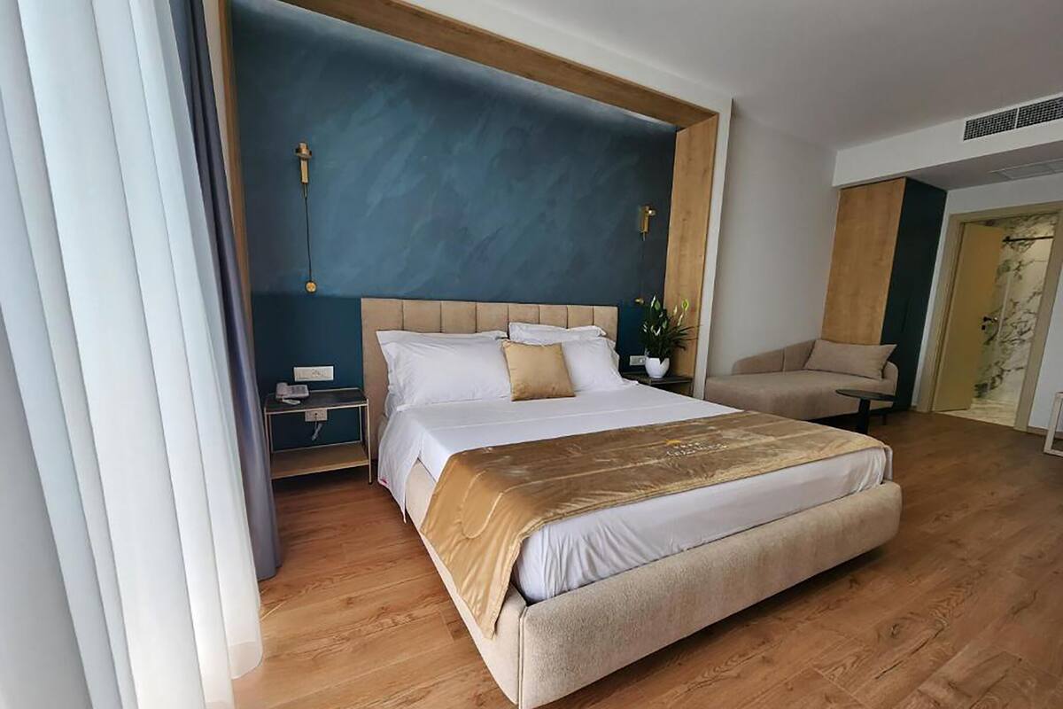 A modern hotel room with a large bed, a wooden floor, a blue accent wall, and a seating area with a chair and table.