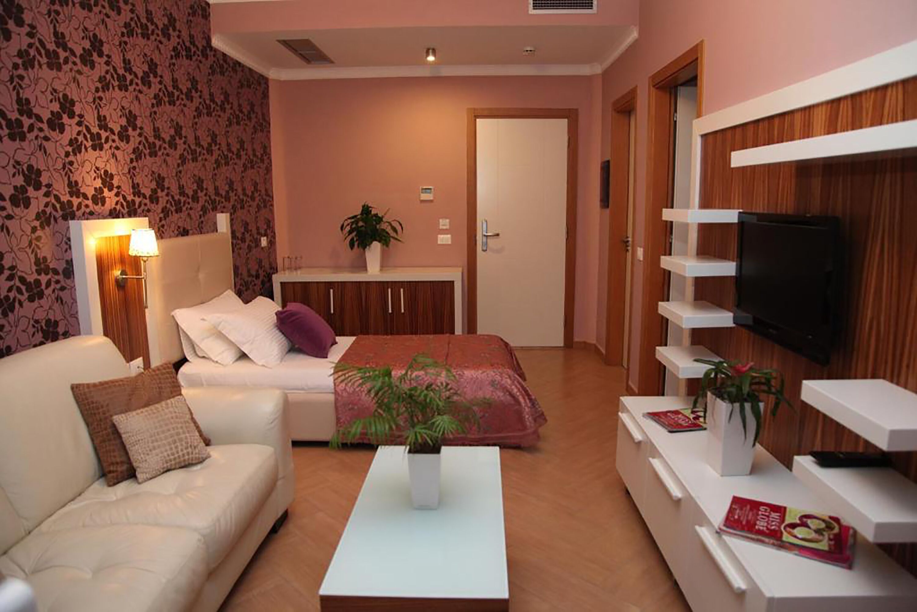 Un salon moderne avec un canapé, une table basse, un téléviseur fixé au mur et un lit recouvert d’une couverture rouge.