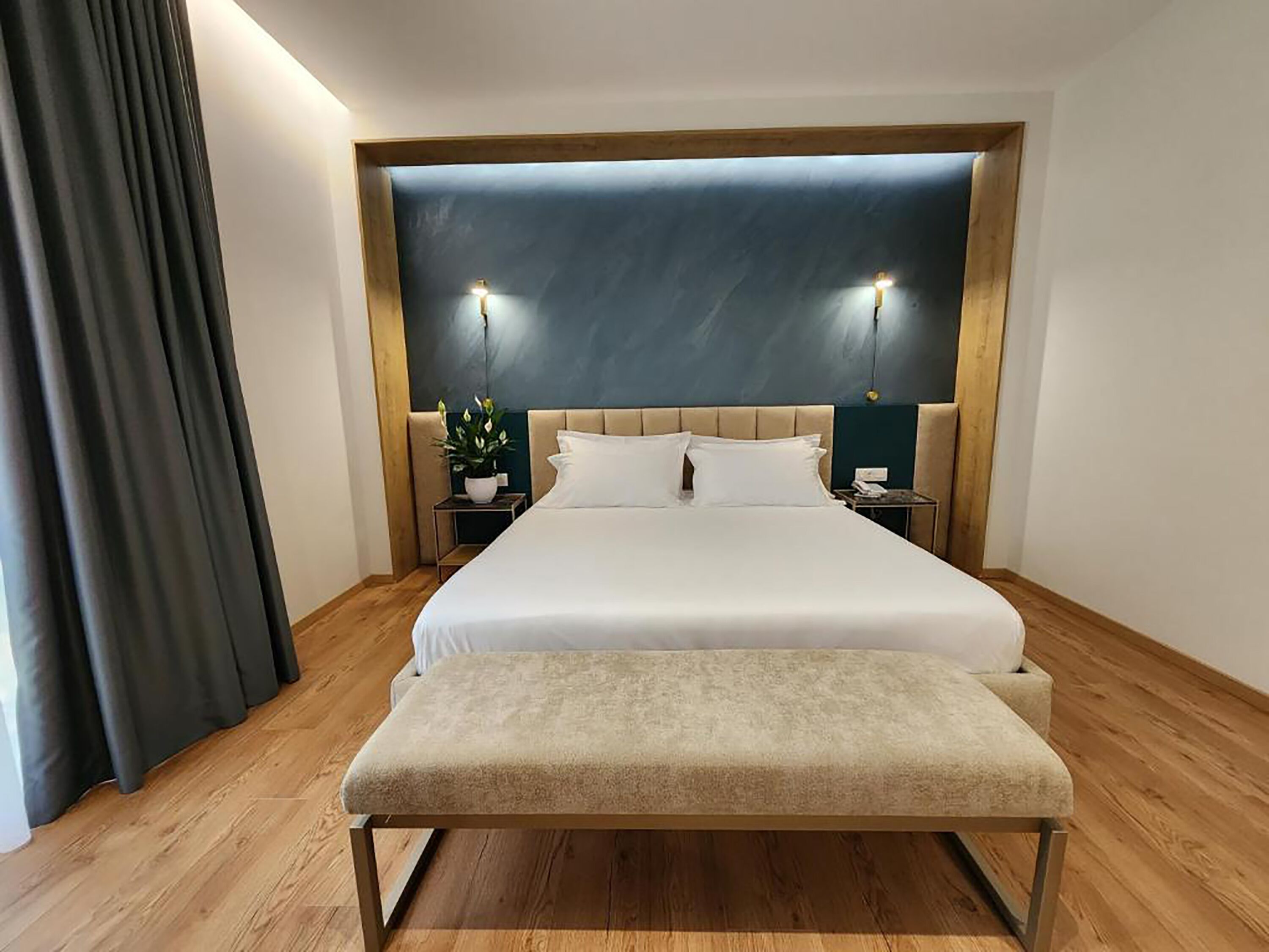 Ein modernes Hotelzimmer mit einem großen Bett, einer Bank, einem Nachttisch mit Lampe und einem Blumentopf.