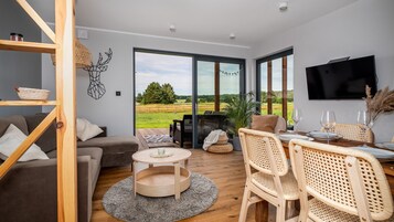 Una sala de estar moderna con un sofá, sillas, una mesa de comedor y un ventanal con vistas a un campo verde.