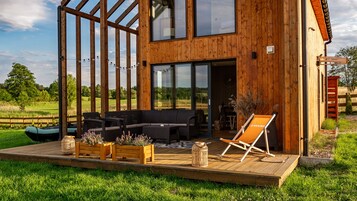 Una cabaña de madera con terraza, asientos exteriores y vistas del paisaje circundante.