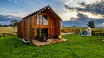 Una cabaña de madera con terraza, tobogán y mobiliario exterior.