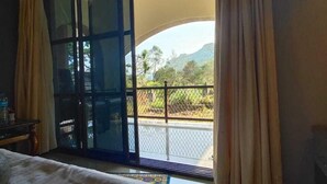 Habitación de hotel con una cama, un ventanal corredero que da a un balcón y un equipo de aire acondicionado en la pared.