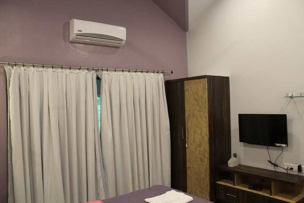 A bedroom with a bed, a wardrobe, a television on the wall, and an air conditioning unit.