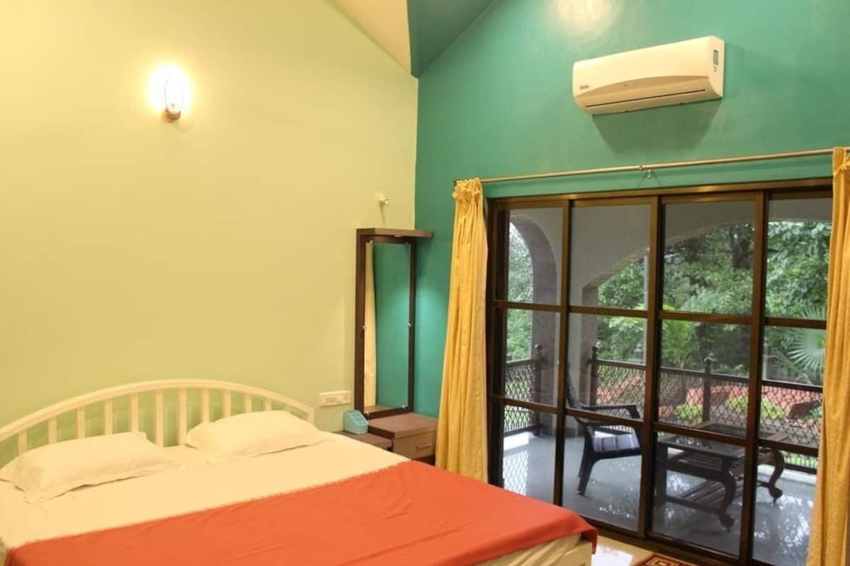 Una habitación con cama, mesita de noche, ventana con cortinas y aire acondicionado.