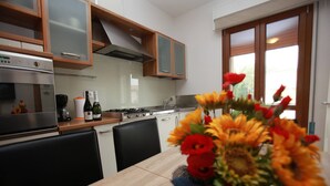 A modern kitchen with wooden cabinets, a built-in oven, and a dining area with a table and chairs. - Renovated Flat Near the Beach - Beahost (Rosolina)