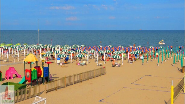 A beach with rows of umbrellas and beach chairs, a playground, and a fence. - Renovated Flat Near the Beach - Beahost (Rosolina)