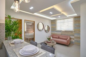 Relax in this stylish living room with a dining area for two, a comfortable sofa, and a beautiful vase of flowers.
