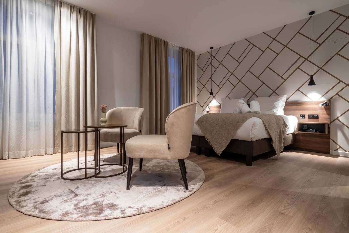Ein modernes Schlafzimmer mit einem Bett, zwei Stühlen, einem kleinen Tisch und einem Nachttisch.
