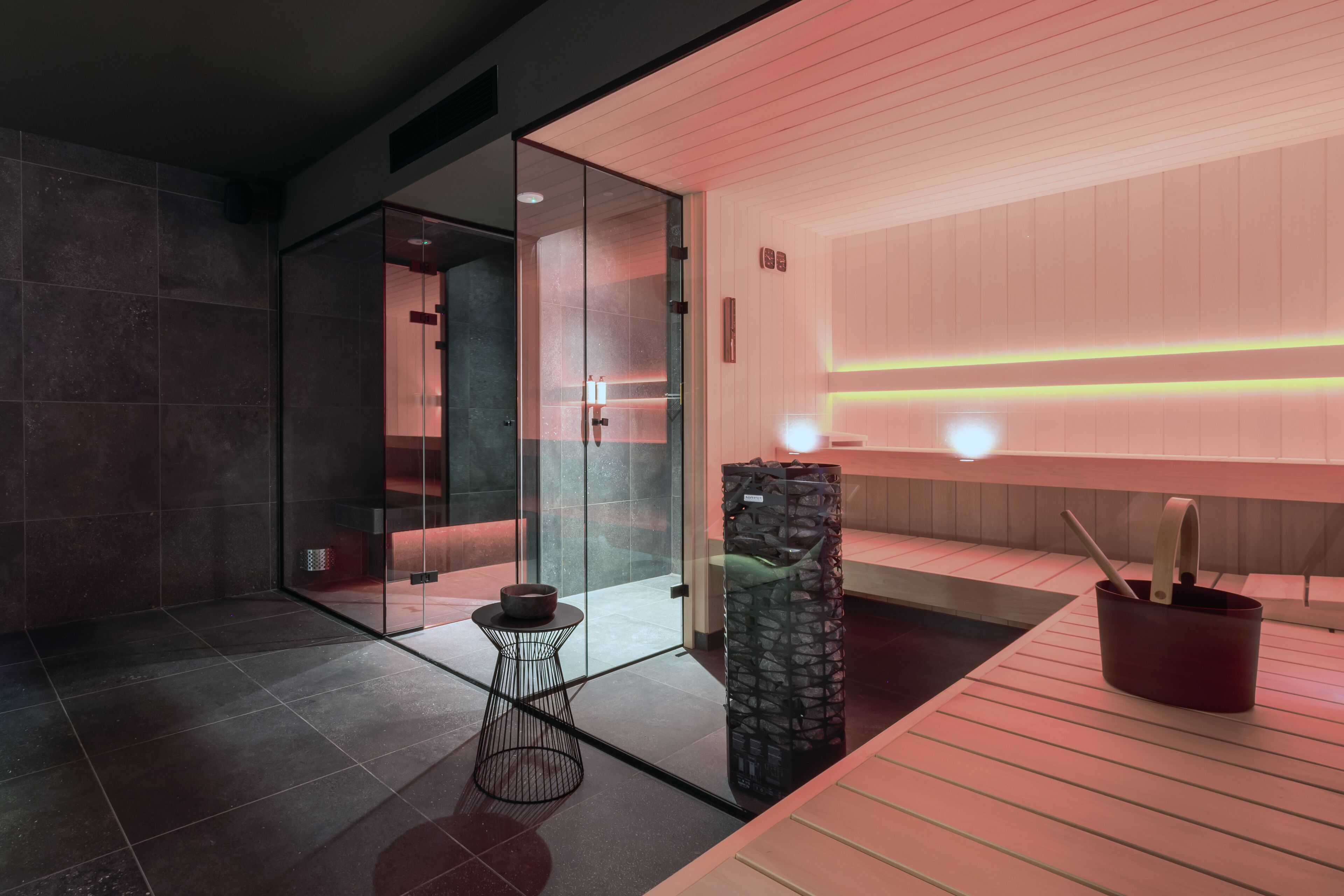 Un baño moderno con cabina de ducha de vidrio, una pequeña mesa redonda y un pilar de piedra.