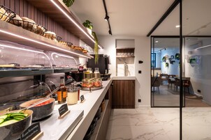 A modern kitchen with a marble countertop, a variety of food items, and a glass partition leading to a dining area.