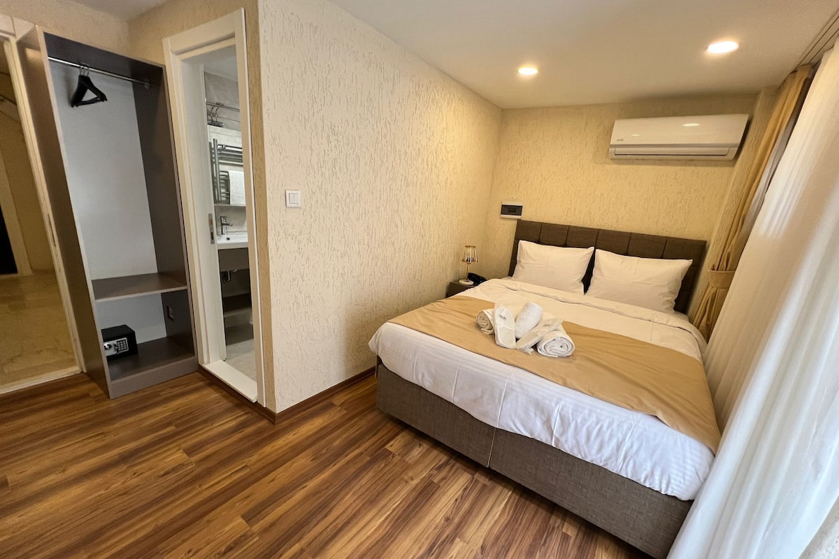 A hotel room with a bed, a wardrobe, a bathroom, and an air conditioning unit.