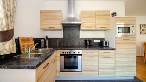 A modern kitchen with a central stove, oven, and microwave, wooden cabinets, and a marble countertop. - Kitz Residenz Six in Kaprun (Kaprun)
