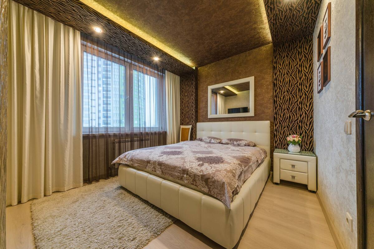 Une chambre à coucher avec un grand lit, une table de chevet, un miroir et une fenêtre avec des rideaux.