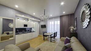 Ein modernes Wohnzimmer mit einer Couch, einem Esstisch und einer Küchenzeile mit weißen Schränken und einer Mikrowelle.