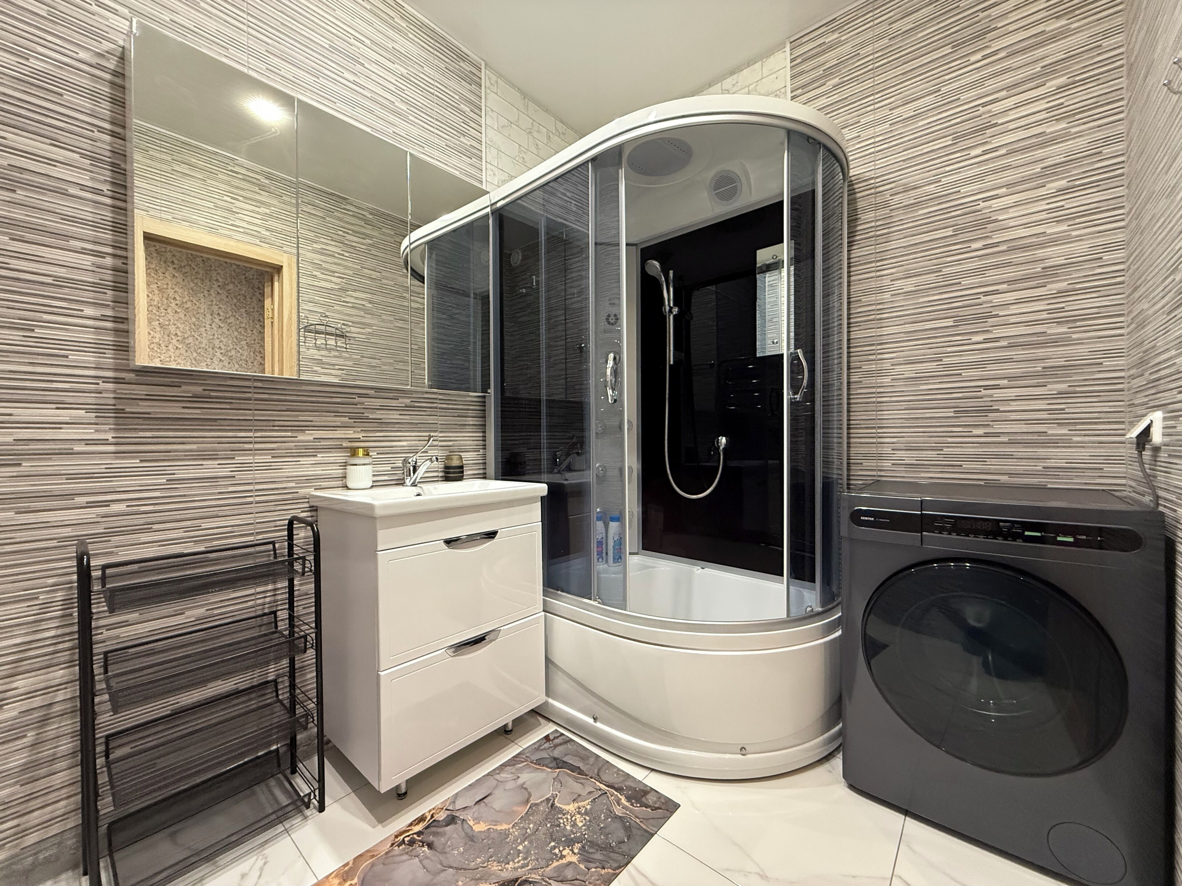 A modern bathroom with a glass-enclosed shower, a built-in washing machine, and a vanity with a mirror.