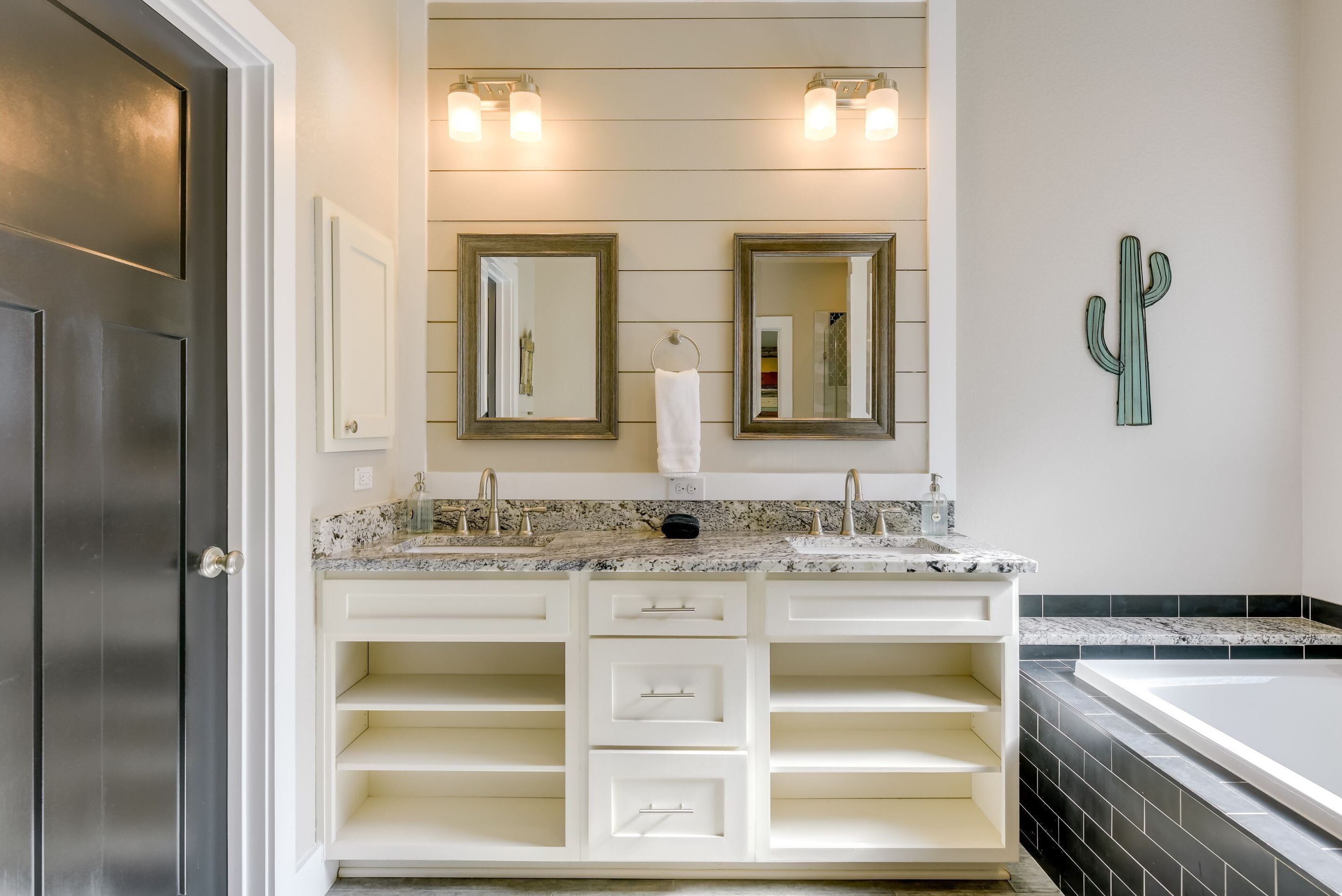 A bathroom with a double vanity, two mirrors, a towel rack, and a cactus decoration.