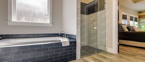 Une salle de bain moderne avec une baignoire carrelée de noir, une douche en verre et un plancher en bois.