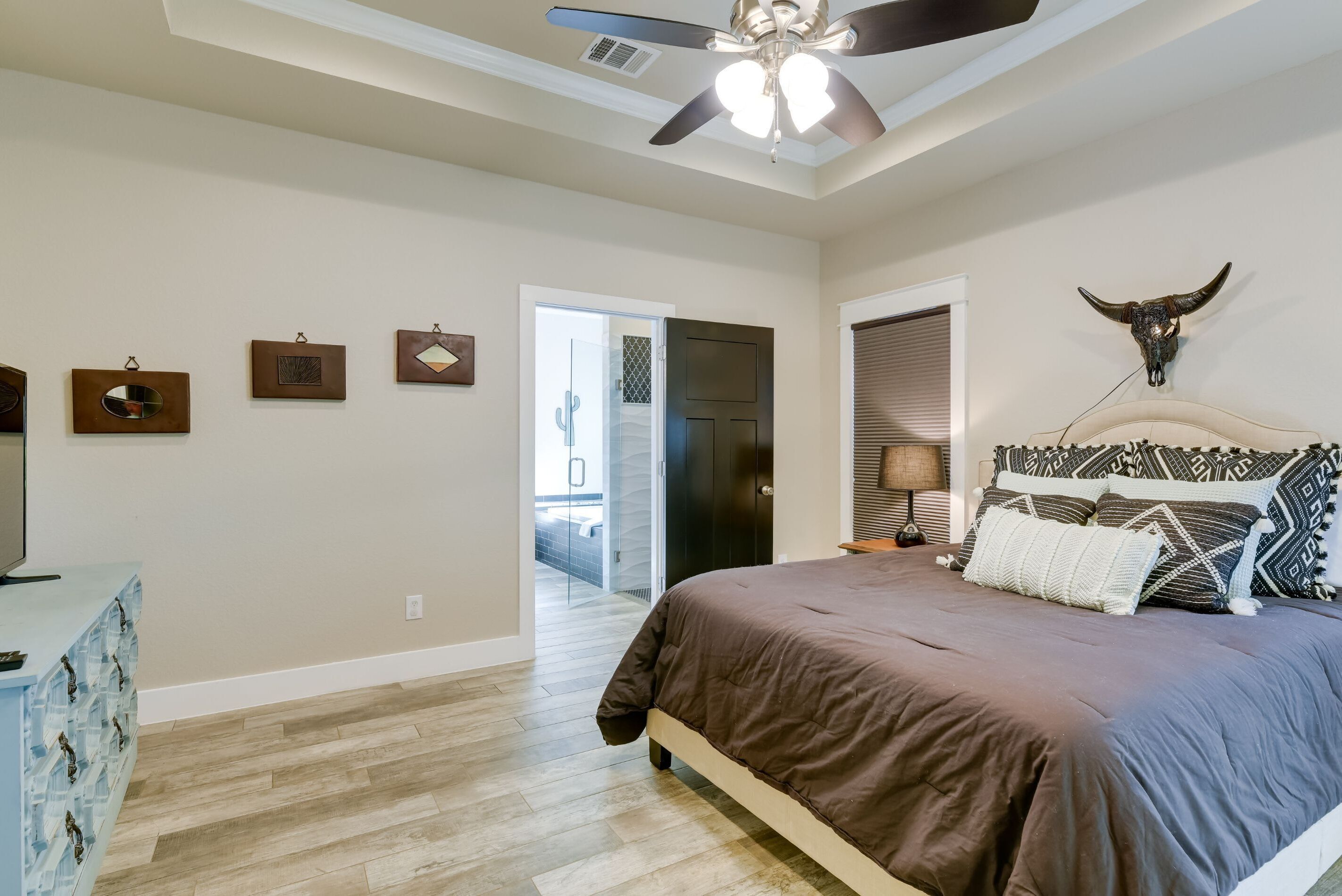 A bedroom with a large bed, a ceiling fan, a bull skull decoration, and a wooden floor.