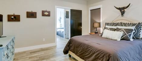 A bedroom with a large bed, a ceiling fan, a bull skull decoration, and a wooden floor.