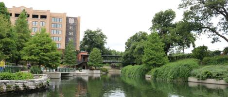 A calm river with a bridge, trees, and a building with a large sign.