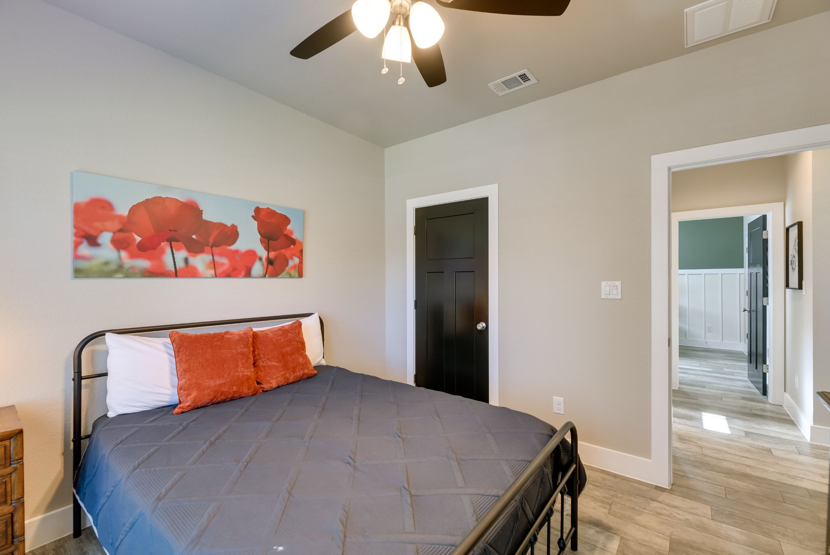 A bedroom with a bed, a ceiling fan, a door, and a hallway leading to another room.