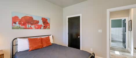 Un dormitorio con cama, ventilador de techo, una puerta y un pasillo que conduce a otra habitación.