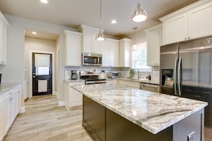 A modern kitchen with white cabinetry, stainless steel appliances, and a large marble island.