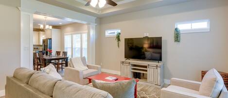 A spacious living room with a large gray sectional sofa, a red coffee table, and a flat-screen TV on a wooden stand.