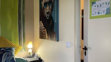 A bedroom with a bed, a nightstand, a lamp, a leopard artwork, a green curtain, and a door with a notice.