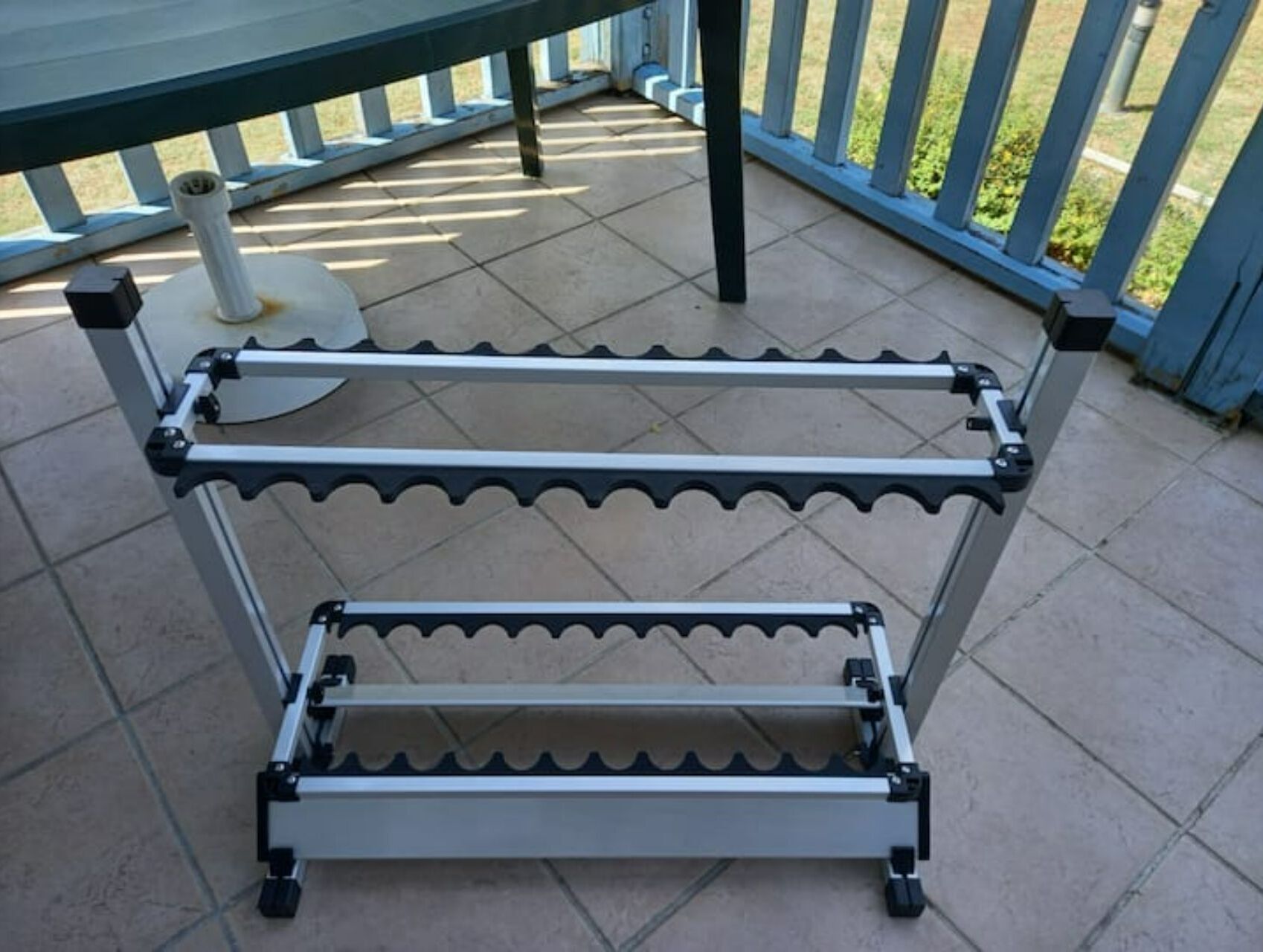 A metal rack with multiple shelves, wheels, and a cylindrical object on a tiled patio.