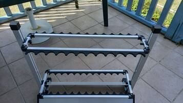 A metal rack with multiple shelves, wheels, and a cylindrical object on a tiled patio.