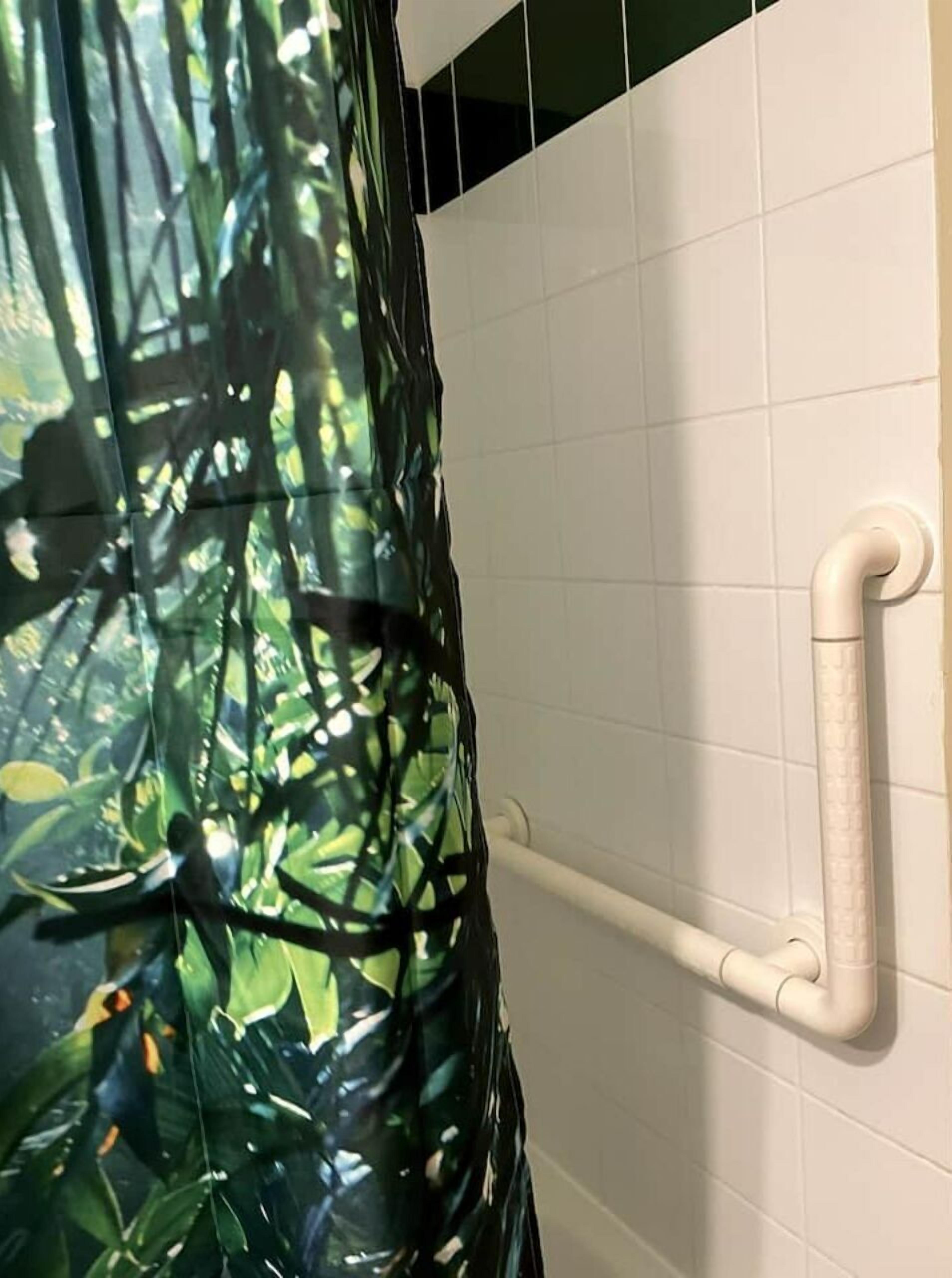 A bathroom with white tiled walls, a white bathtub, and a shower curtain with a jungle print.
