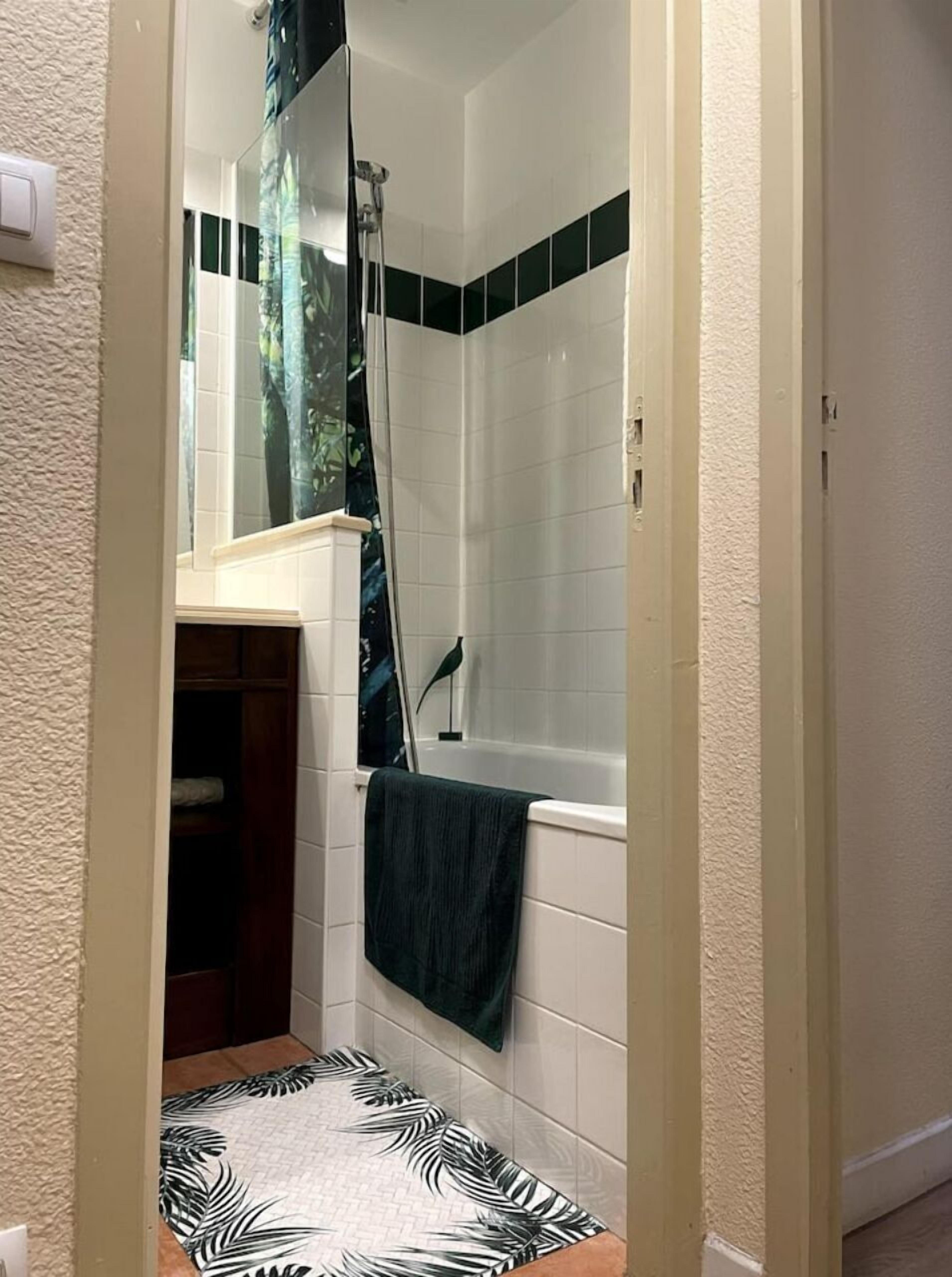 A bathroom with a bathtub, a shower, and a toilet. There is a towel hanging on the wall and a patterned mat on the floor.